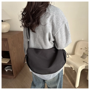 Rear view of a large black nylon crossbody bag with side drawstring worn by a model