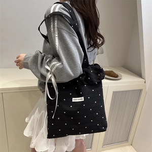 Sac fourre-tout noir à fleurs blanches avec froufrous et étiquette porté à l'épaule