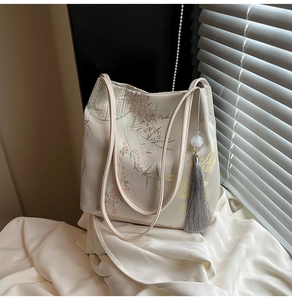 Detail of vintage canvas tote bag featuring floral embroidery and grey tassel pendant