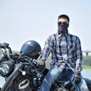 Close-up of rider in blue checkered shirt with neck gaiter and gloves on a retro motorcycle