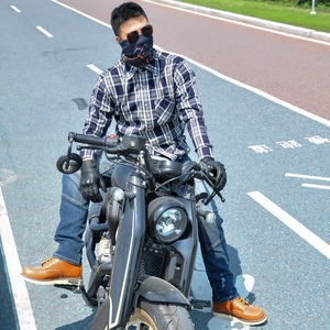 Outdoor shot of a biker in a blue plaid shirt, denim jeans, and brown leather boots