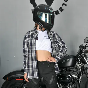 Motorradfahrerin in kariertem Hemd und schwarzer Schutzhose neben einem Motorrad-Klassiker