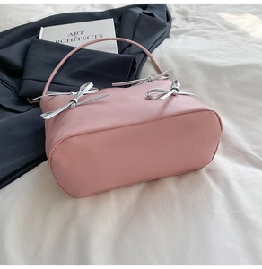 Detail of light pink bucket bag with silver bow decoration and matte leather finish