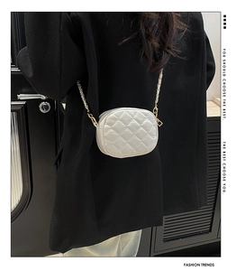Détail d'un sac rond blanc matelassé avec bandoulière en chaîne dorée sur blazer noir