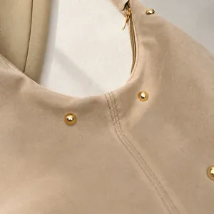 Detail view of beige suede shoulder bag featuring golden metal studs and fine stitching