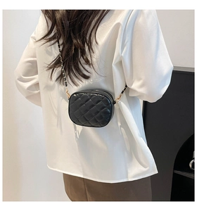 Quilted black mini round crossbody bag with chain strap shown on model from side view