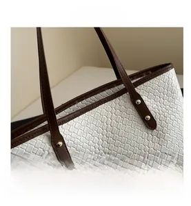 Close-up of white woven leather tote bag featuring brown leather strap and gold metal rivets