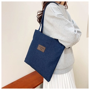 Deep blue denim tote bag with leather patch detail worn by model in casual street style