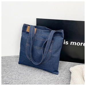 Detail of dark blue denim tote bag featuring orange stitching and front pocket detail