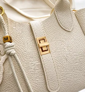 Détail du sac seau en cuir grainé avec fermoir rotatif doré et pendentif gravé M