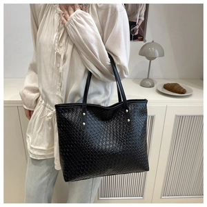 Close-up of black woven tote bag with gold stud details on shoulder strap and PU texture