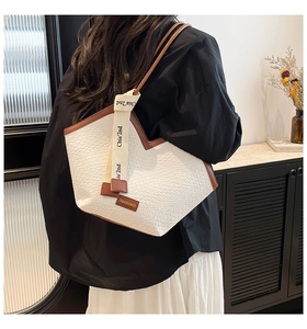 Detail of white woven tote bag with brown leather trim and stylish lettering ribbon