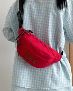 Detail of red nylon waist bag featuring adjustable black strap and brown zipper puller