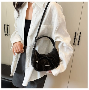 Détail d'un sac bandoulière noir brillant avec nœud coulissant et logo argenté