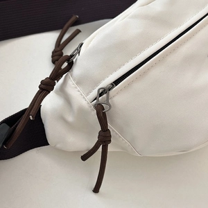 Close-up of cream crossbody bag featuring brown braided zipper pull and fine stitching