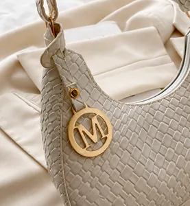 Detail der weißen geflochtenen Tasche mit goldenem M-Anhänger und eleganter Ledertextur