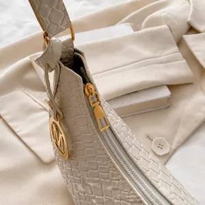 Detail der cremefarbenen Tasche mit Kroko-Prägung und goldenem M-Anhänger