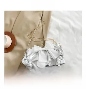 Mini silver metallic bag with a white bow shown next to a smartphone for size comparison