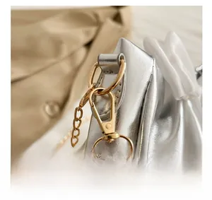 Detailed macro view of gold-tone metal lobster clasp and chain on a silver leather handbag