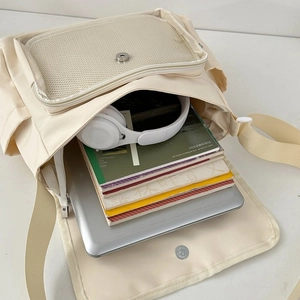 Ruime beige schoudertas interieur met laptop, boeken en grote koptelefoon