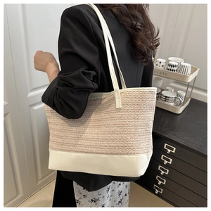 Détail du sac cabas en paille montrant la texture tissée beige et les anses en similicuir blanc
