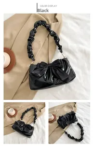 Detail of black patent leather handbag featuring a large velvet bow and ruched handle