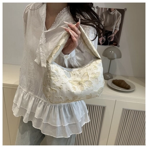 Détail de la broderie papillon dorée sur un sac à bandoulière en satin blanc crème chic