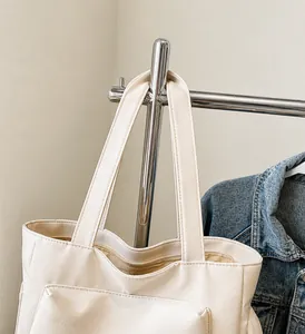 Dettaglio dei lunghi manici lisci e della tasca anteriore della borsa tote beige