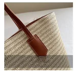 Close-up of beige and green woven tote bag with brown leather handles and white stitching