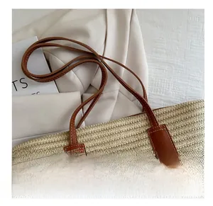 Detail of woven straw tote bag with brown leather handles and a pink butterfly charm