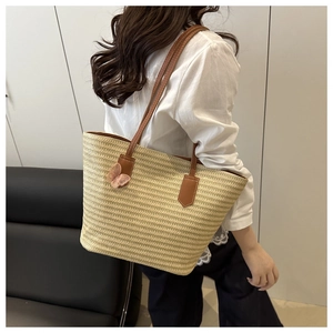 Detail of woven straw tote bag with brown leather straps and pink butterfly charm