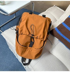 Top view of a tan oxford fabric backpack with drawstring closure on a grey sofa