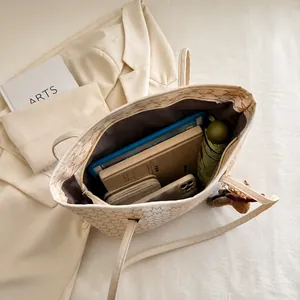 Vista superior del amplio bolso tote beige con monograma, tableta y cuaderno