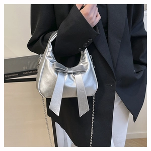 Detail van een zilveren handtas met grote strik en metalen ketting in spiegelglas