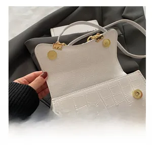 Detail showing white crocodile pattern texture and gold magnetic clasp on the handbag