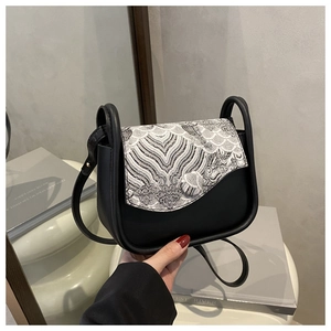 Detail of saddle bag showing wave pattern embroidery and matte leather texture in a soft setting