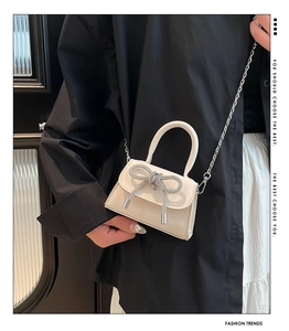 Close-up of beige mini bag featuring a sparkling rhinestone bow and metal chain strap