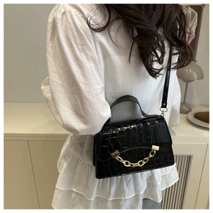 Détail du sac bandoulière noir texture crocodile avec chaîne dorée et boucle métal