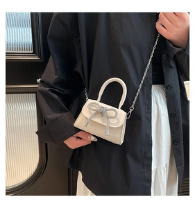 Detail of a mini ivory crossbody bag with a sparkling rhinestone bow and silver chain strap
