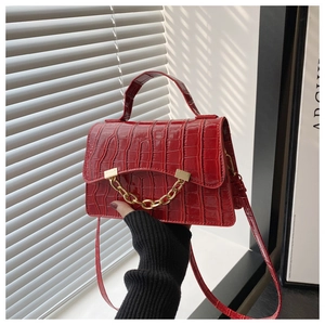 Détail du sac rouge à motif croco avec chaîne dorée sous la lumière naturelle des stores
