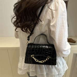 Sac bandoulière noir brillant à motif crocodile avec chaîne dorée sur chemisier blanc