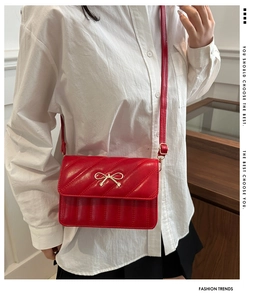 Detail van rode gewatteerde leren crossbodytas met een gouden strikdecoratie