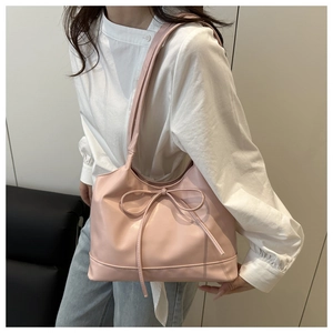 Detailed view of a pink tote bag with a bow knot carried by a model in casual attire