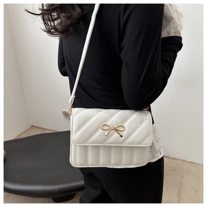 Detail van witte gewatteerde crossbodytas met gouden strik en slanke schouderband