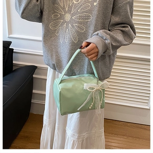Close-up of mint green handbag featuring delicate white lace bow and pearl decoration