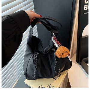 Detalle de bolso hobo de nailon negro plisado con un tierno colgante de perro marrón