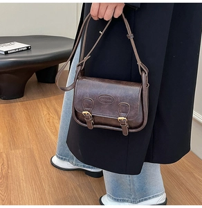 Detail of vintage dark brown saddle bag with faux oil wax texture and twin strap buckles