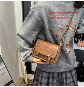 Detail of vintage brown textured leather crossbody bag with decorative buckles and strap