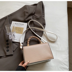 Detail of twist top handle and golden hardware on beige and white contrast handbag