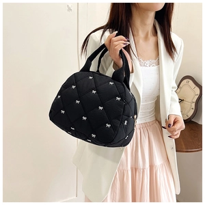 Detail of black quilted tote bag with white bow embroidery and sturdy handles